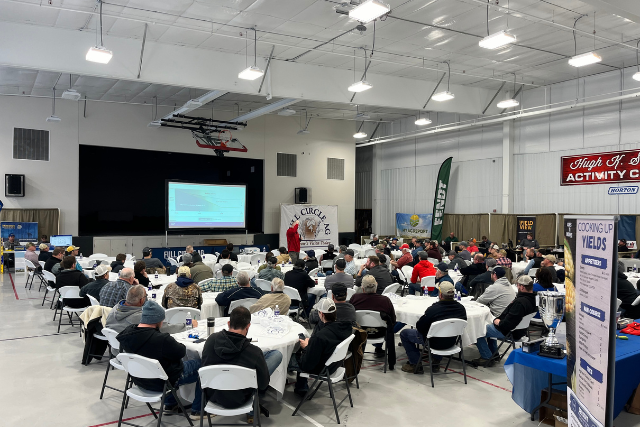 event center meeting with a room full of people sitting at tables listening to a speaker