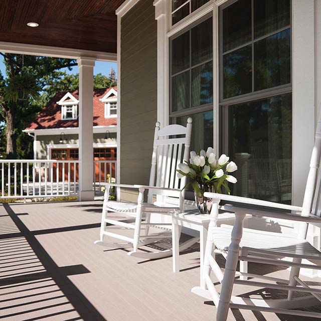 Rocking chairs on a porch, a table with a vase of flowers sits between them.