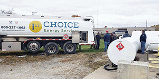 Group of People Standing Near Fuel Truck and Storage Tanks