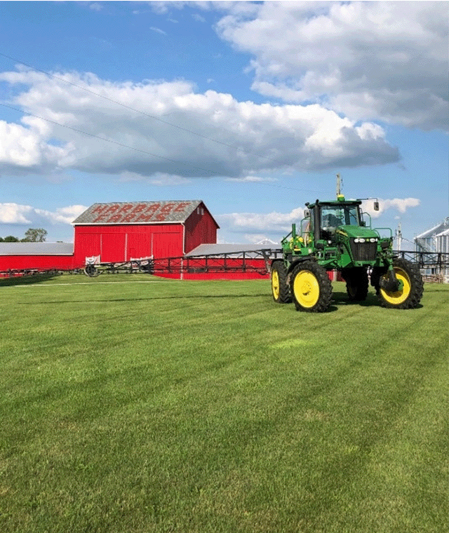 John Deere Tractor with Boom Sprayer Sitting In Front of Barn