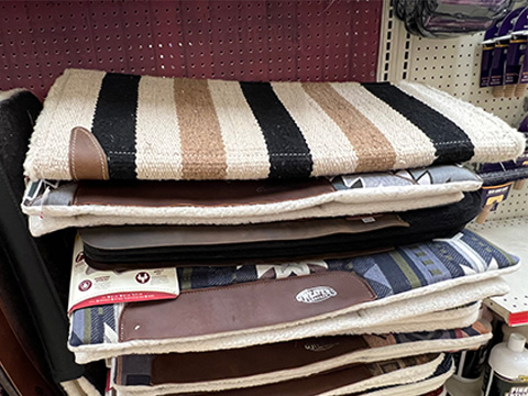 A stack of saddle pads on a shelf.