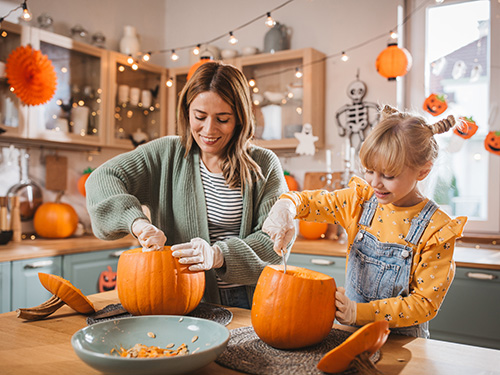 A mom and daughter scooping seeds out of pumpkins in the kitchen
