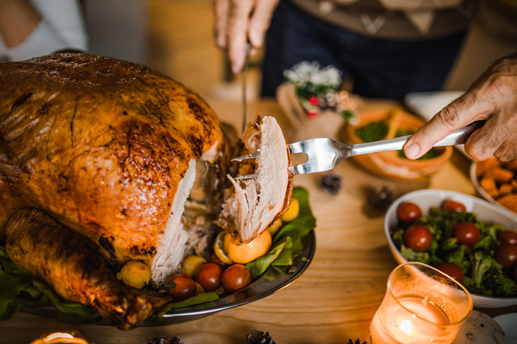 Up close shot of someone carving a turkey on Thanksgiving. There are several side dishes on the table as well.