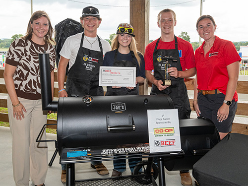 Winners of the grill off posing with their trophy in front of a grill.